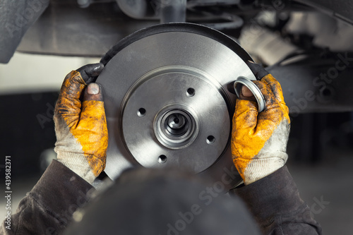 Closeup male tehnician mechanic greasy hands in gloves install new car oem brake steel rotor disk during service at automotive workshop auto center. Vehicle safety checkup and maintenance concpet