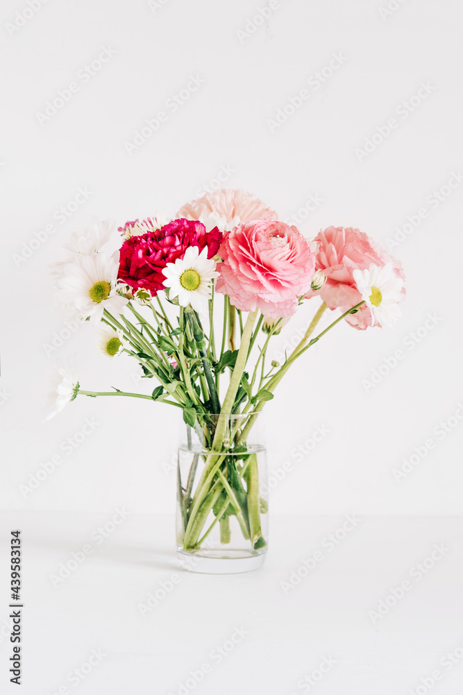 A bouquet of fresh spring flowers in a glass vase on a white table.