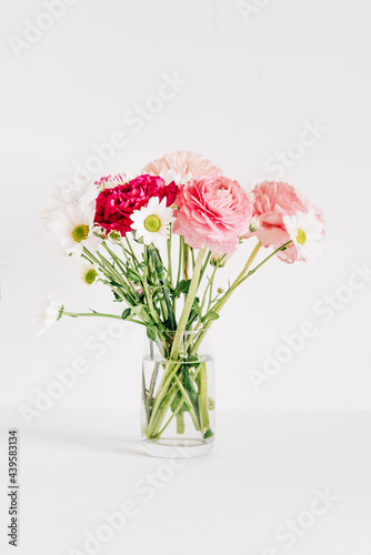 A bouquet of fresh spring flowers in a glass vase on a white table.