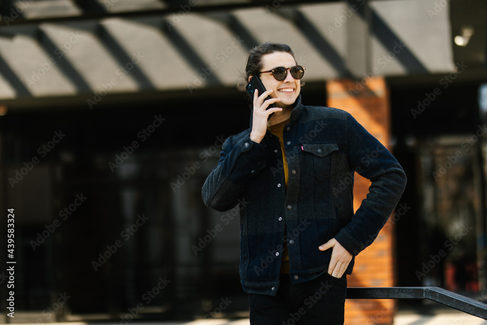 Handsome young businessman walking on the street on the riverside while talking on his phone