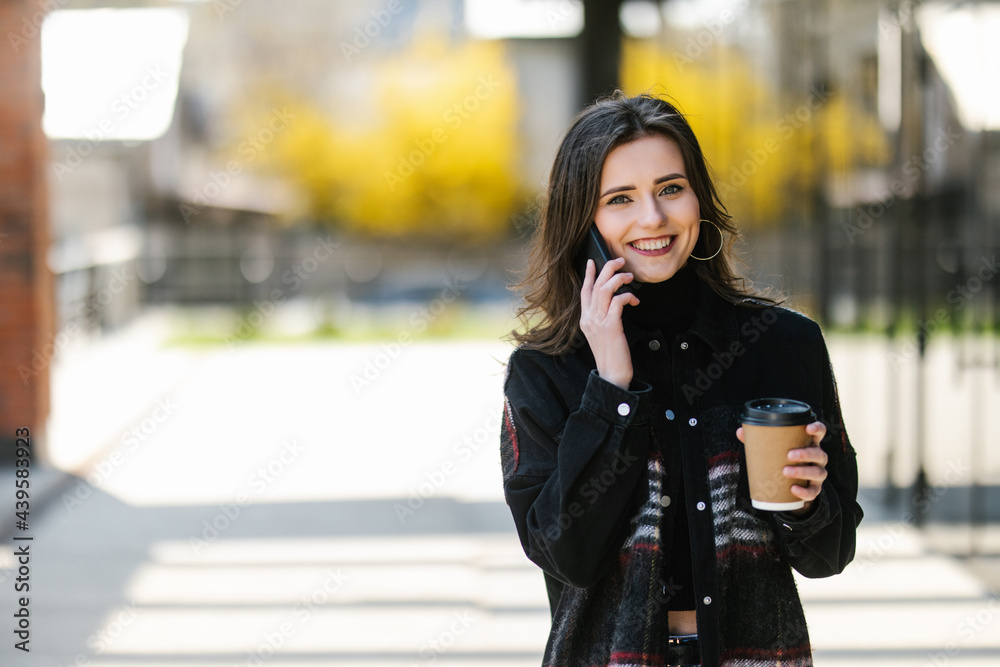 Smiling woman talking on the mobile phone and drinking coffee on the street