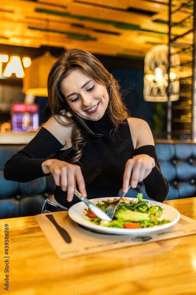 Portrait of a smiling woman eating food and talking on mobile phone in cafe