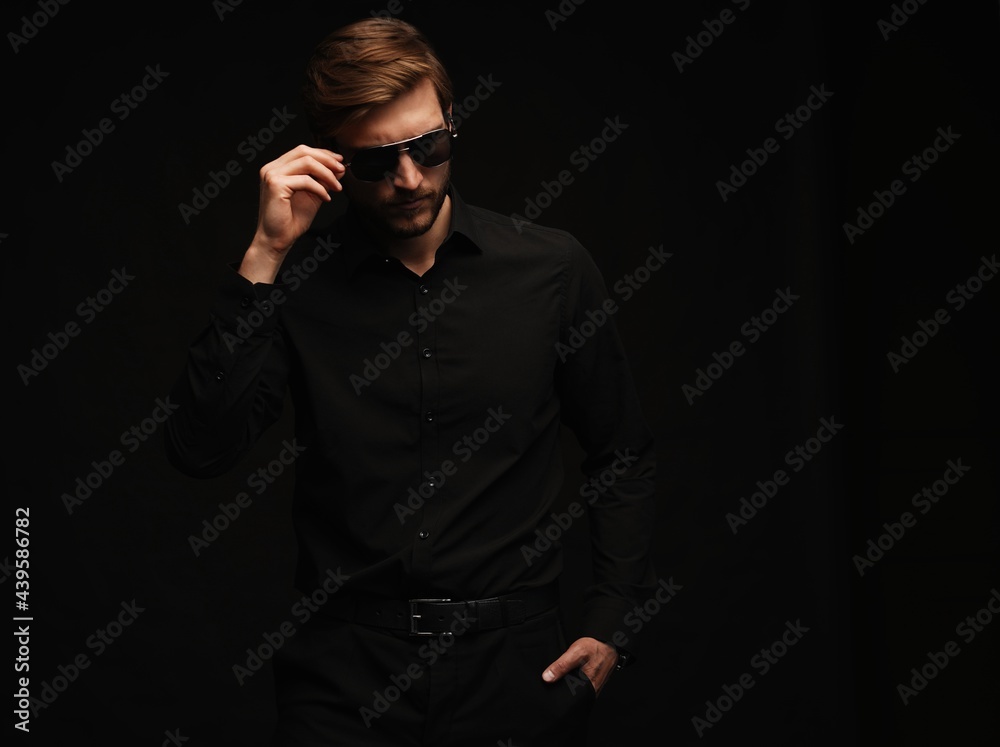 Men in full suit. Confident young businessman in sunglasses standing isolated on black.