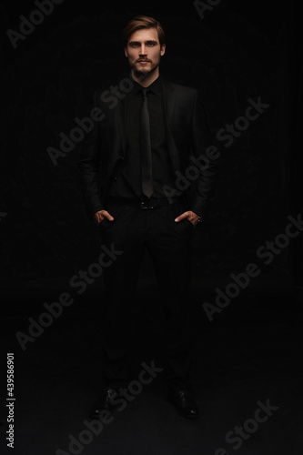 Young man in black suit full body portrait against black background.