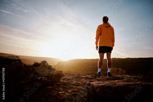 Rear view of young male athlete watching beautiful sunrise after morning run during mountain trail
