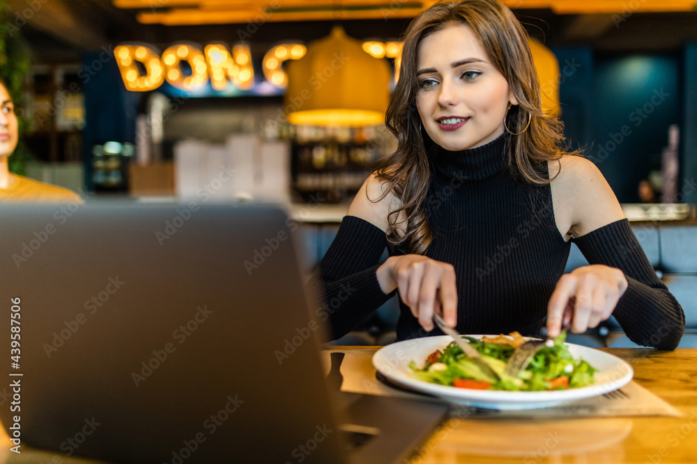 Young pretty woman sitting with a laptop in a cafe and eating breakfast