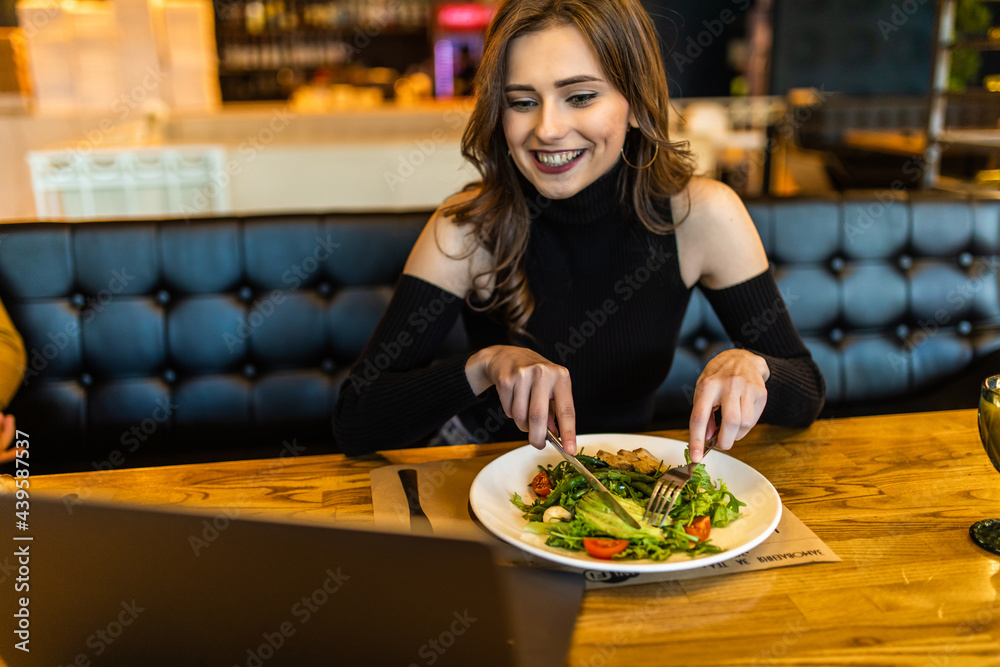 Young woman enjoying salad sitting with laptop at the cafe
