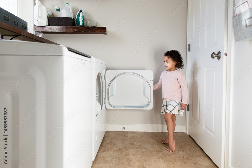 Girl opens dryer in laundry room Girl opens dryer in laundry room
