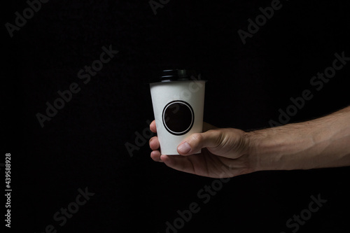 Paper coffee cup with lid on a black background. There is a place for an inscription or a logo. Coffee to go. Hand holds a paper cup.