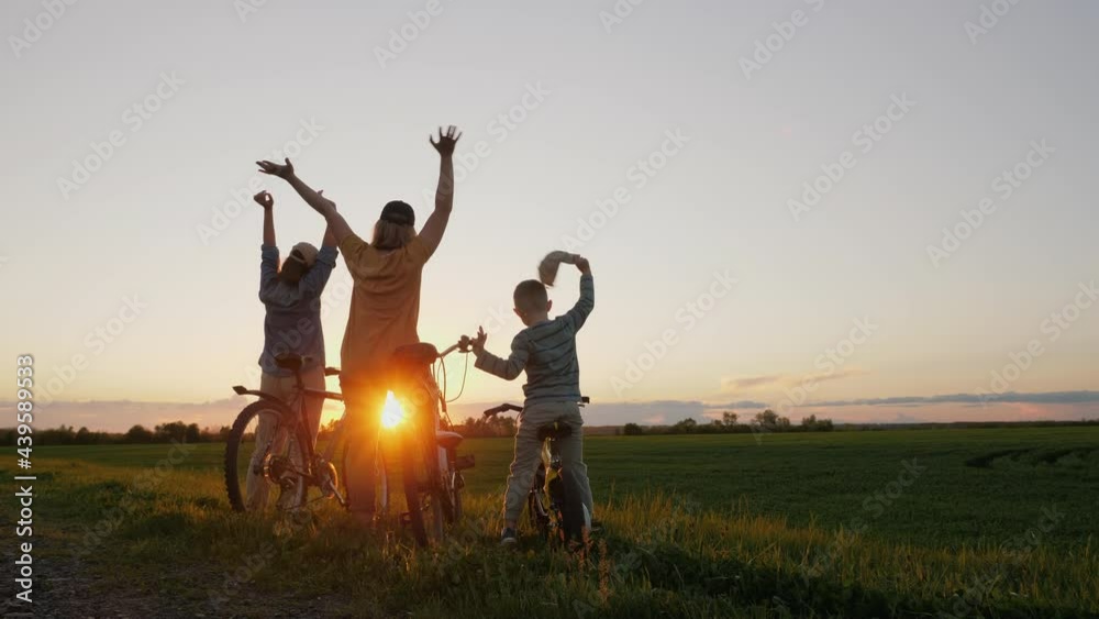 Woman with two children with bicycles standing at sunset and waving with hands. Enjoying amazing scenery. Woman with two children with bicycles standing at sunset and waving with hands. Enjoying amazing scenery.