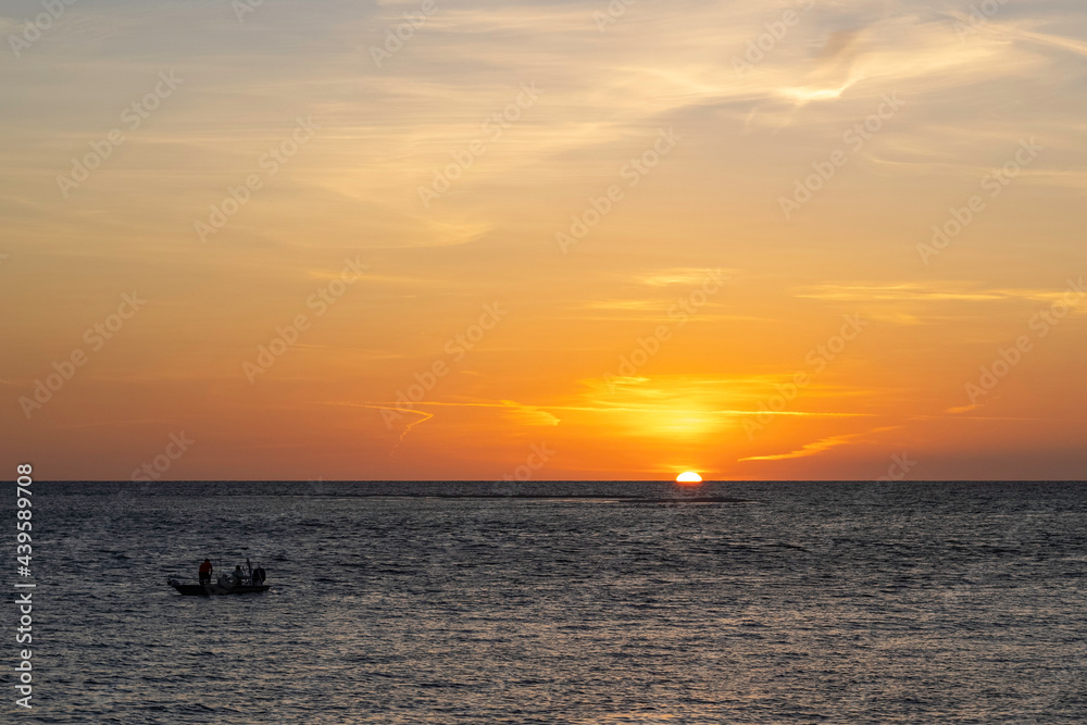 Sun sets on the ocean with a fishing boat in silhouette.