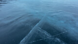 Smooth blue ice surface. Close-up. Full frame. Crossing cracks are visible going into the depth, traces of skates. Baikal