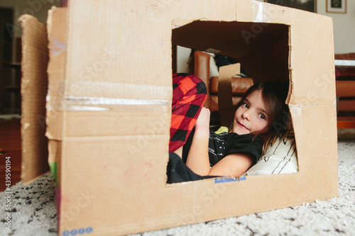 little girl lays down inside cardboard box fort photo