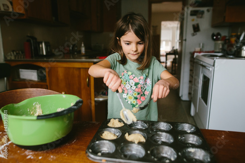 A young girl mixes ingredients to bake muffins at home photo