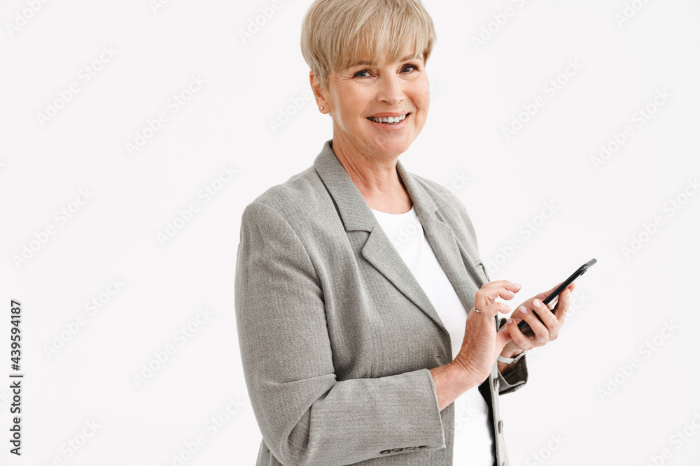 European mature woman in jacket smiling while using mobile phone European mature woman in jacket smiling while using mobile phone