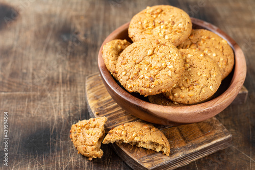 Healthy homemade oatmeal cookies with peanuts in a wooden bowl on a brown kitchen table closeup