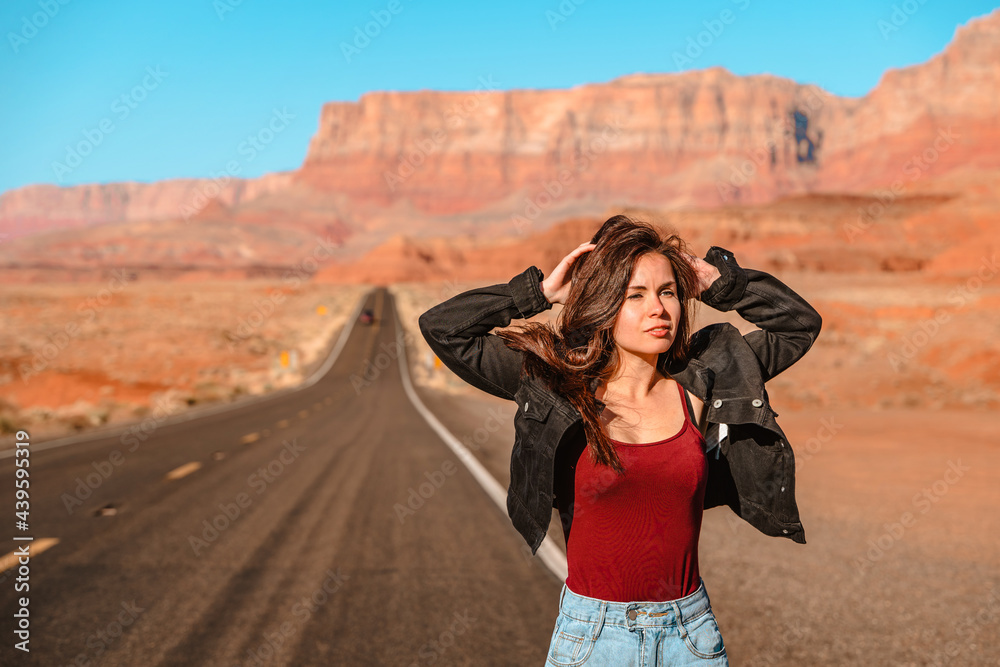 A beautiful long-haired woman in a denim jacket walks along an empty road in the desert in Arizona with a view of red rocks