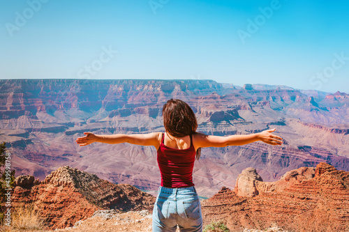 Beautiful young woman stands with her arms open in front of a view of the Grand Canyon, Arizona