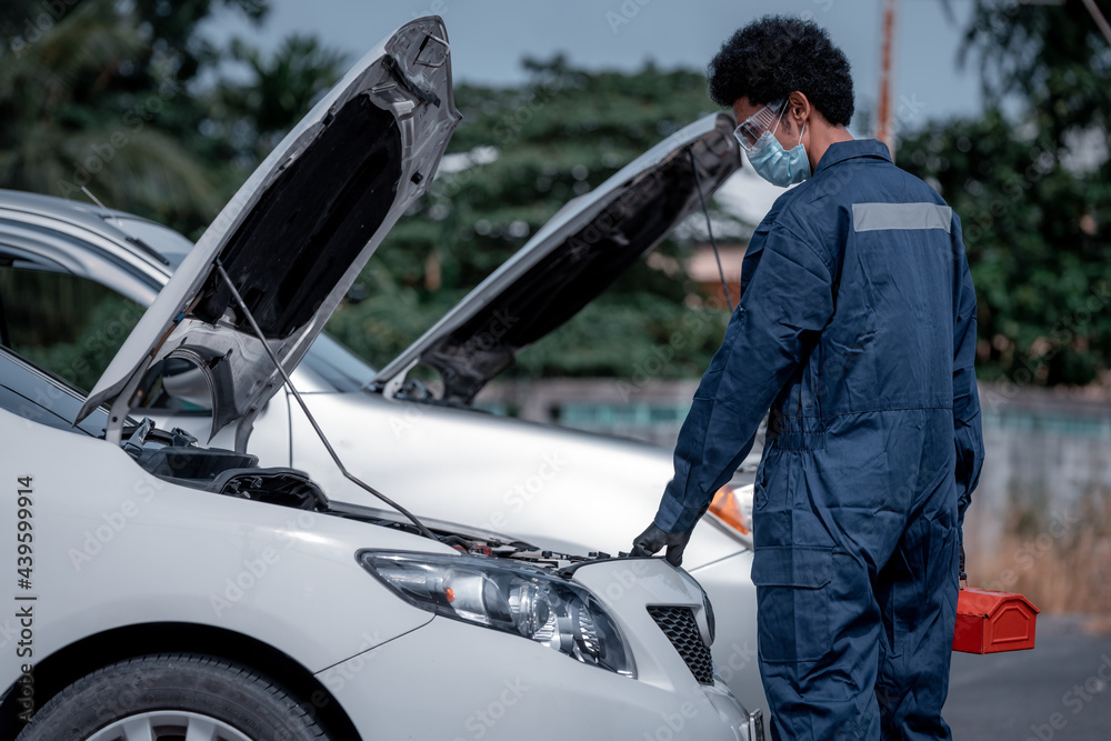 Car mechanic open car hood repairs and check problem system hand to maintenance and fixed in garage .he wearing face mask to protect for virus and pollution.