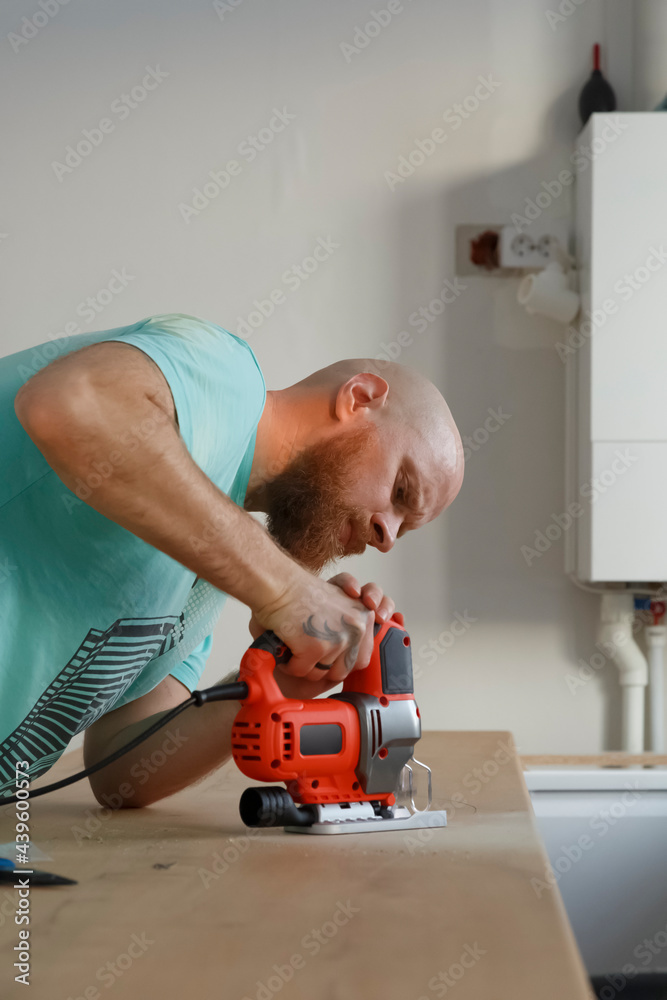 Bearded male woodworker cutting wood with electric jigsaw Bearded male woodworker cutting wood with electric jigsaw