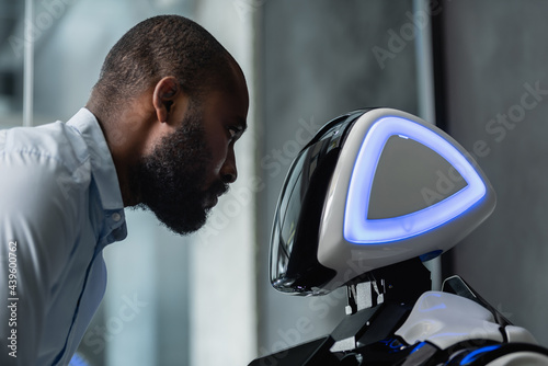 african american engineer looking at humanoid robot in office photo