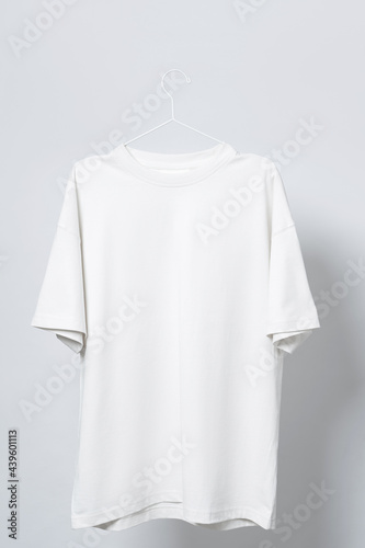Blank white t-shirt hanging on a hanger against gray background