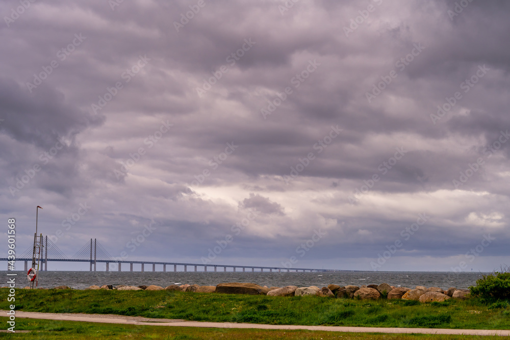 A beautiful, dramatic sky over the ocean. A lawn and stones in a wave breaker in the foreground. Picture from Malmo, Sweden