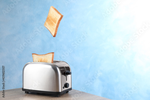 Bread slices popping up from modern toaster on wooden table. Space for text