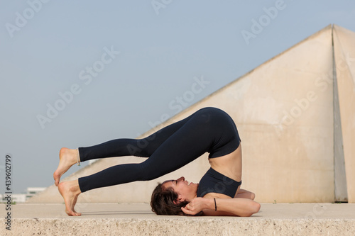 Thin athletic middle eastern woman stretching in a Yoga pose. Shot in an empty urban park in early morning sunlight.