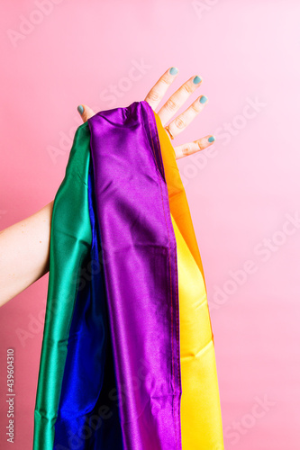 Woman hand with green painted nails holding a lgbtq flag on colorful flat background. lesbian concept