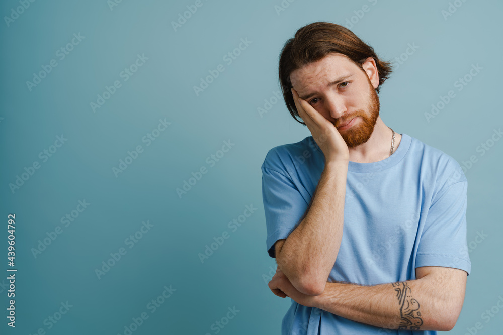 Young ginger man with beard propping his head while looking at camera Young ginger man with beard propping his head while looking at camera