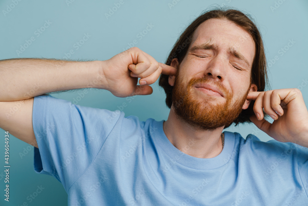 Obraz premium Young ginger man with beard plugging his ears while posing on camera