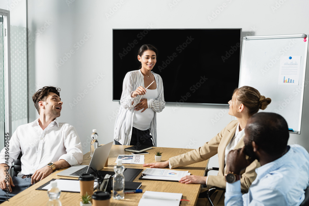 pregnant african american businesswoman smiling while talking to multiethnic colleagues pregnant african american businesswoman smiling while talking to multiethnic colleagues