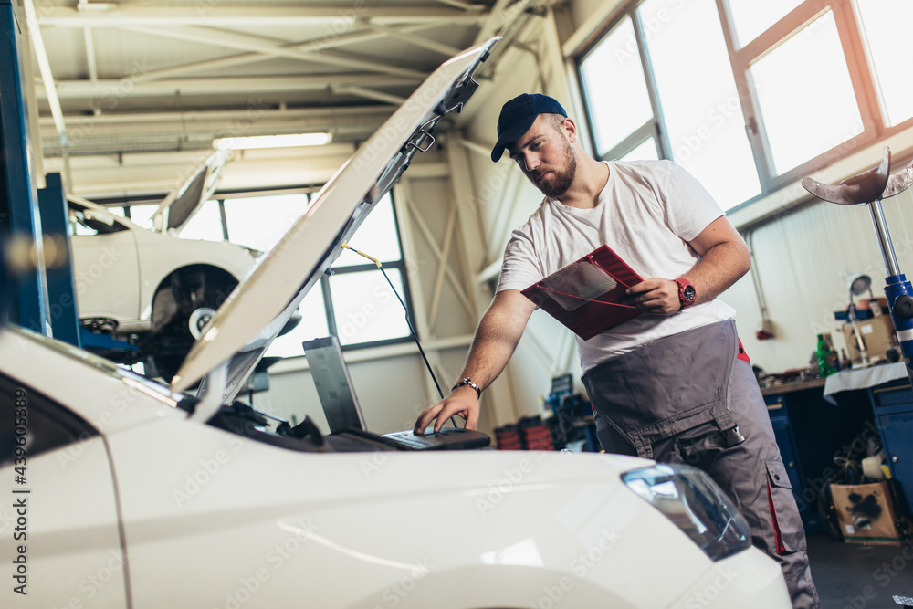Professional car mechanic working in auto repair service using laptop.