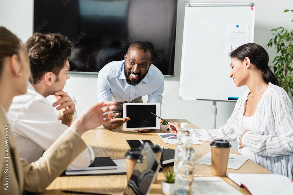 smiling african american businessman showing digital tablet with blank screen during meeting with colleagues smiling african american businessman showing digital tablet with blank screen during meeting with colleagues
