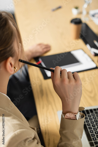 partial view of young businesswoman holding pen in conference room  blurred background