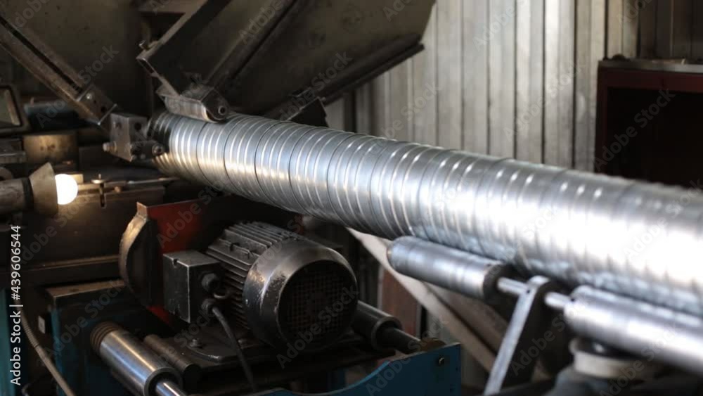 The machine produces a stainless steel ventilation pipe. Plant for the production of ventilation pipes. A worker at a factory makes metal ventilation pipes. The machine produces a stainless steel ventilation pipe. Plant for the production of ventilation pipes. A worker at a factory makes metal ventilation pipes.