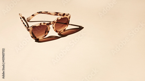 Single women sunglasses on a beige background with a strong shadow