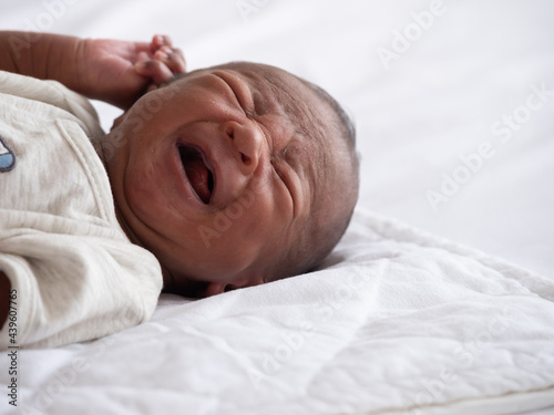 African American baby boy crying on a white bed.