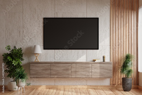 TV on a white concrete wall in a modern living room with a lamp and books placed on a wooden cabinet and decorated with a plant pot on the wooden floor.3d rendering.