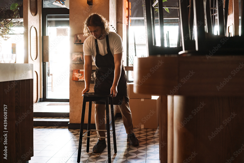 Young white cafe employee in apron working indoors