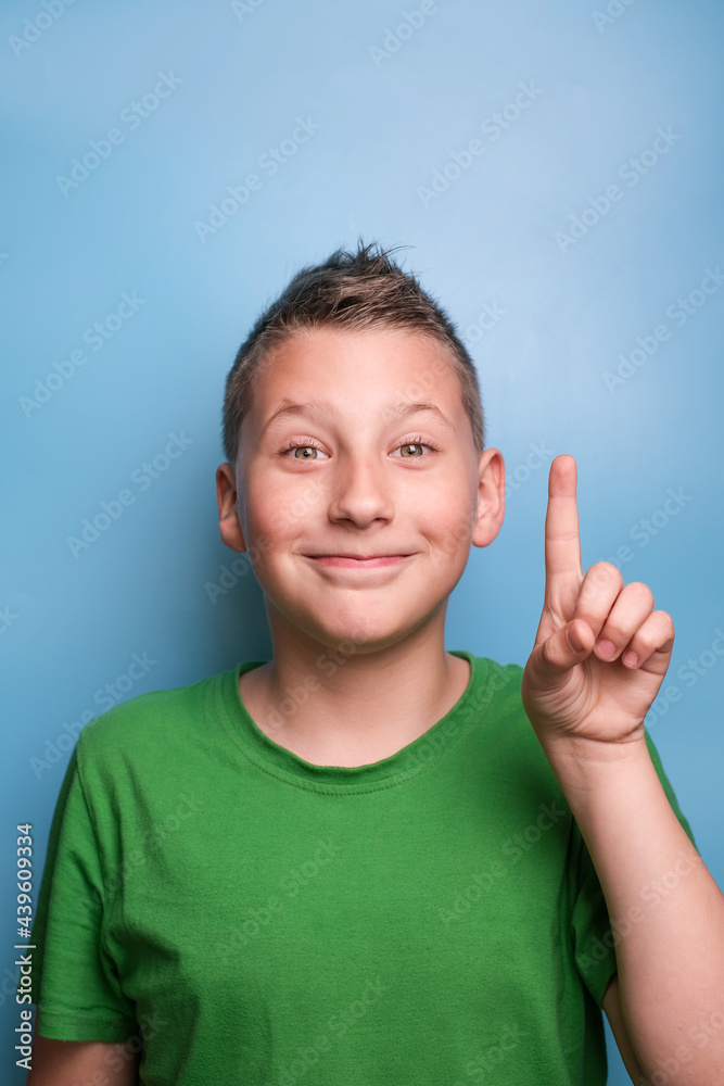 Head shot of emotional adorable boy showing have an idea sign by finger. Portrait on blue background Head shot of emotional adorable boy showing have an idea sign by finger. Portrait on blue background