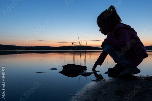 Silhouette of a child touching the lake water at sunset, blue hour. Calmness and silence on the lake.