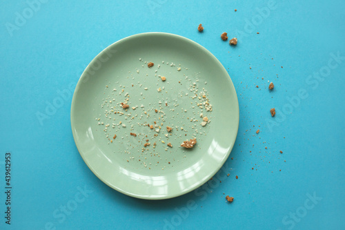 Emty white plate with some crumbs on light blue background. Finished party and holidays concept. photo
