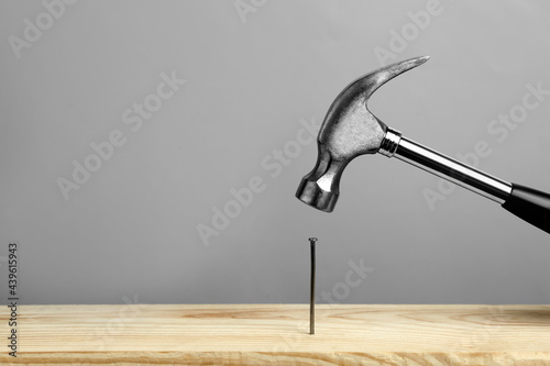 Fotografia, Obraz Hammering nail into wooden surface against grey  background, space for text