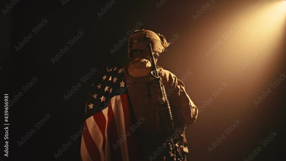 USMC soldier standing with his back to us in the dark holding USA national flag