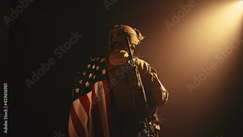 USMC soldier standing with his back to us in the dark holding USA national flag