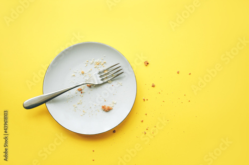 Conceptual image of the end of the holiday. Empty round plate with crumbs and fork on it on yellow background. photo