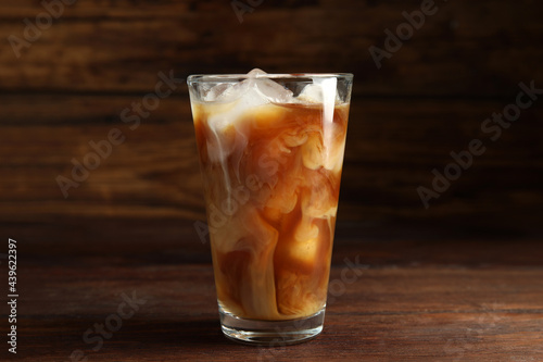 Glass of coffee with milk and ice cubes on wooden table