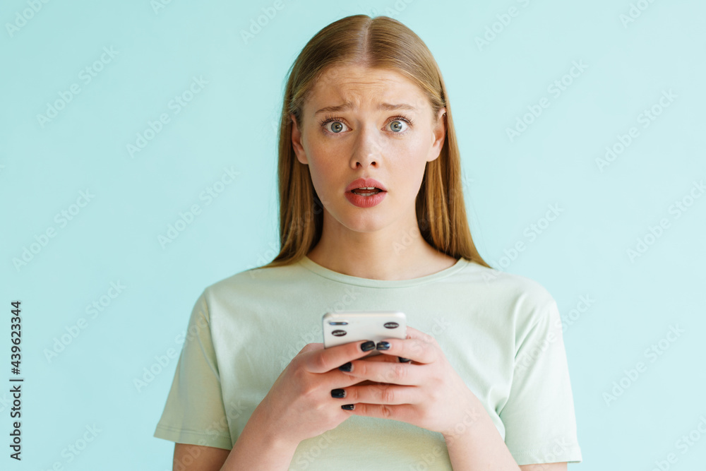 Young scared woman looking at camera while using cellphone Young scared woman looking at camera while using cellphone
